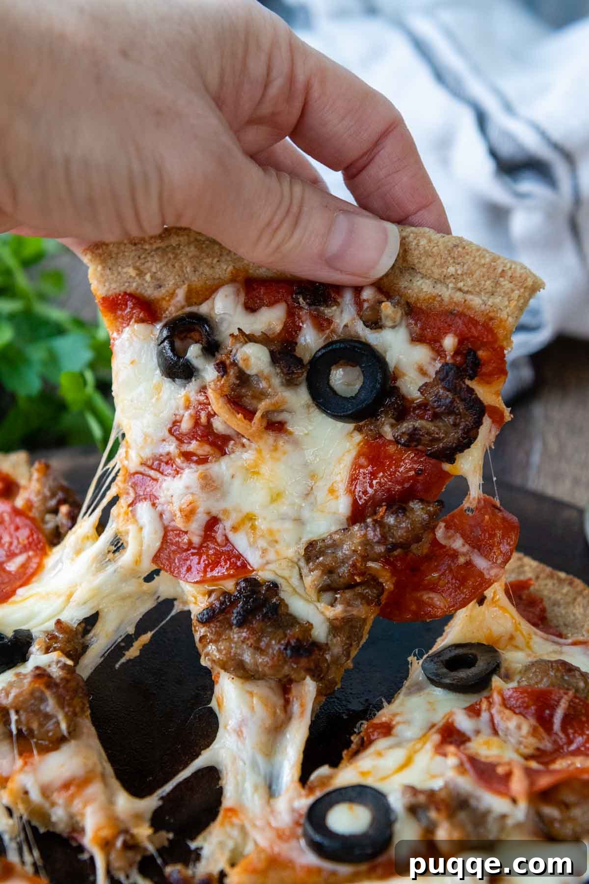 A delicious slice of almond flour pizza being pulled, with cheese stretching and dripping down.