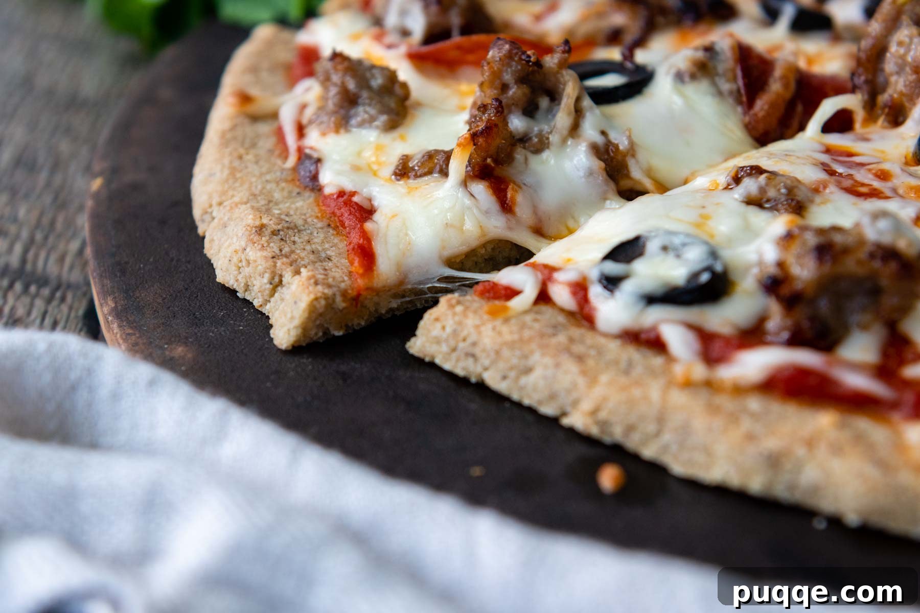 Close-up overhead shot of a perfectly baked almond flour pizza crust on a pizza stone, with melted cheese and toppings.