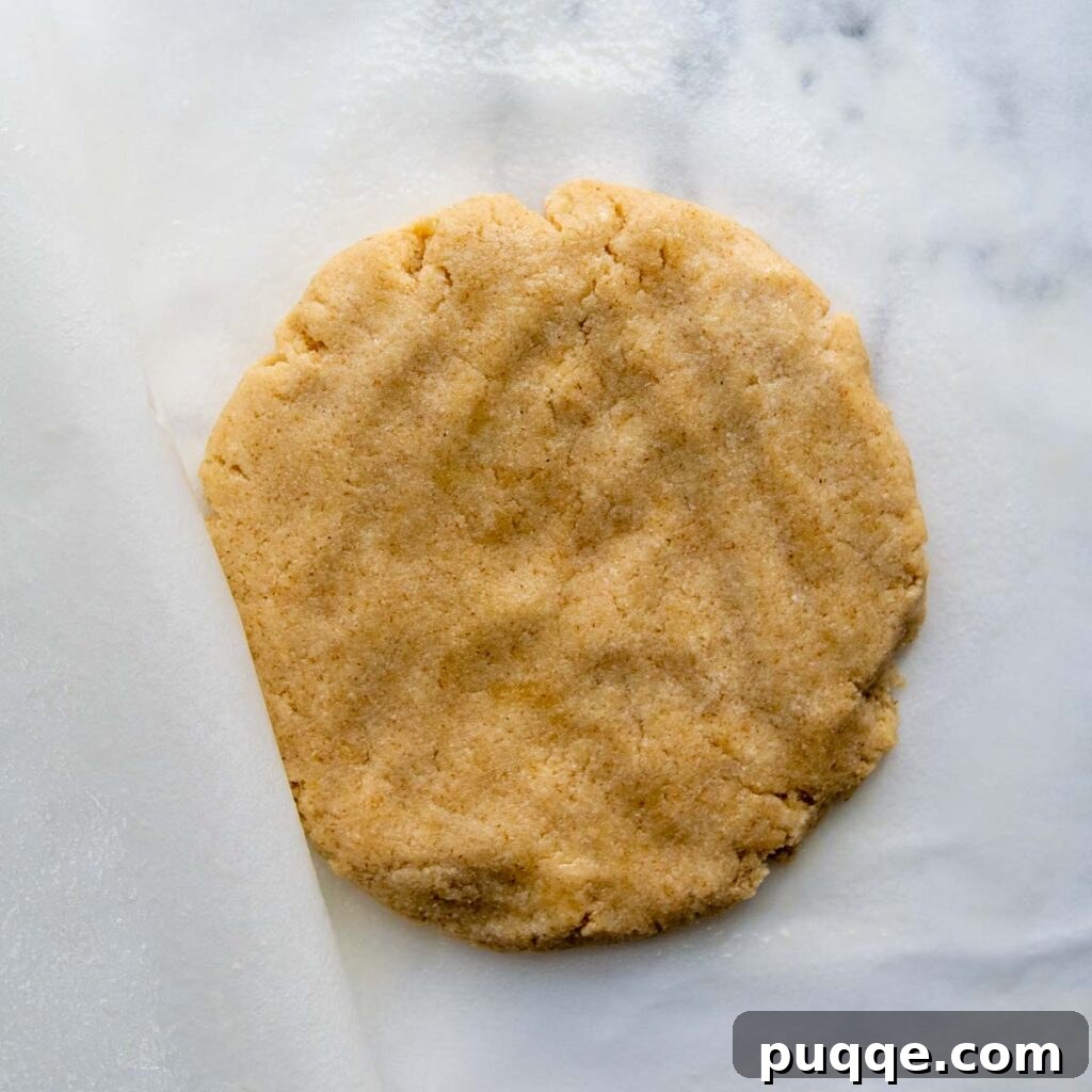 Almond flour pizza dough patted into a thick disc between parchment papers.