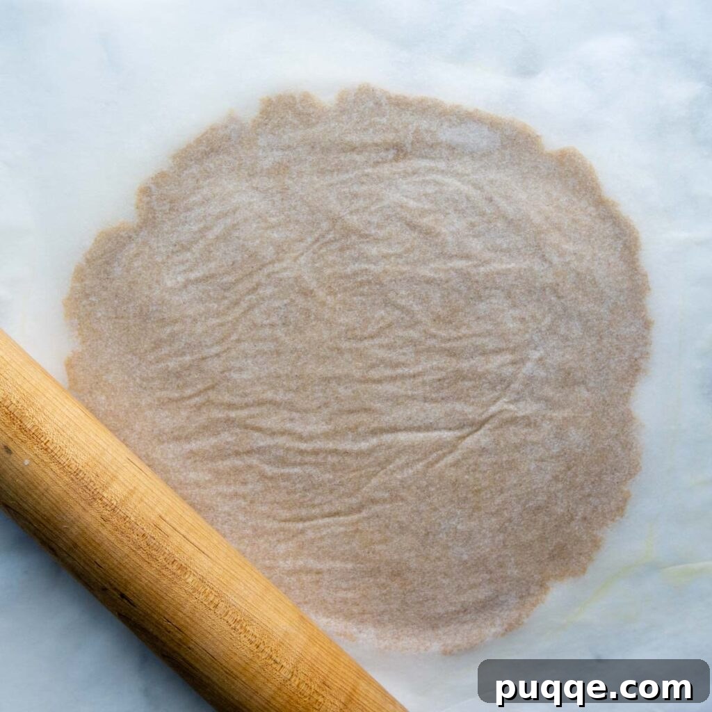 Pizza crust being rolled out between two sheets of parchment paper with a rolling pin.