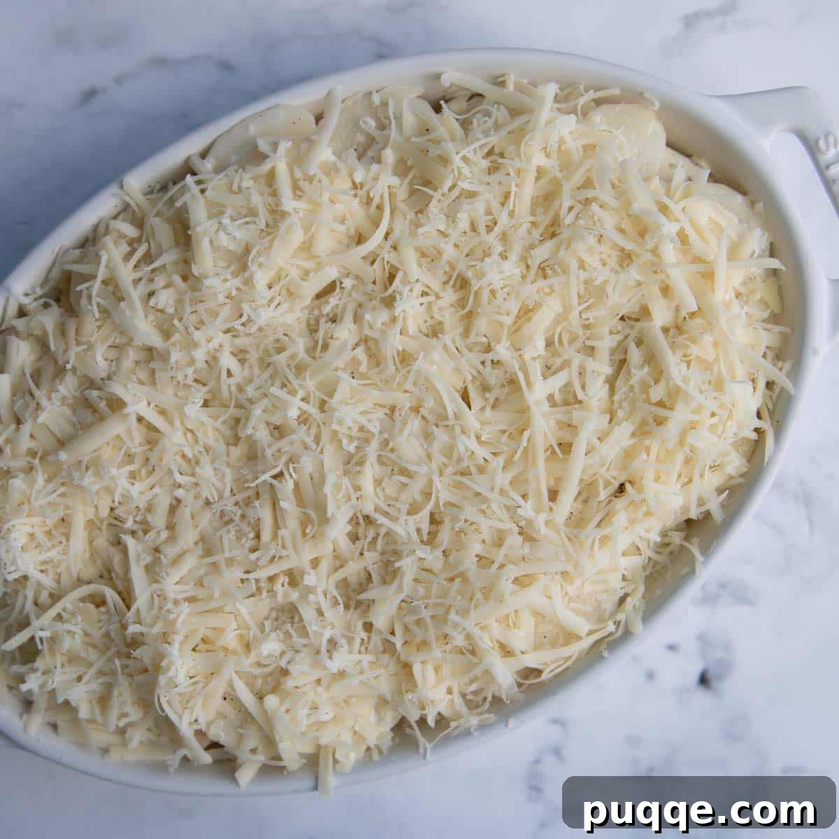 An unbaked au gratin potato casserole, showing layers of sliced potatoes, creamy sauce, and shredded cheeses in a white baking dish.
