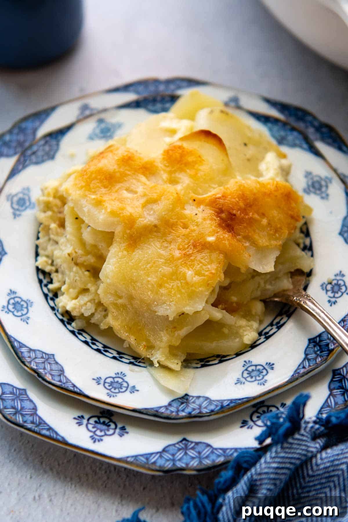 A generous serving of golden-brown au gratin potatoes on a white and blue patterned plate, showcasing the crispy cheese crust and tender layers.
