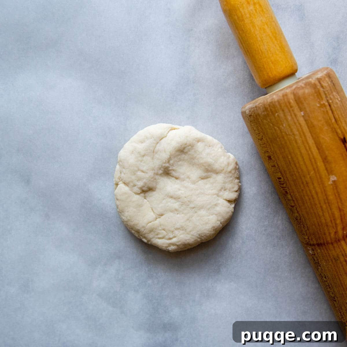 A thick disc of gluten-free dough with a rolling pin beside it, ready to be flattened.