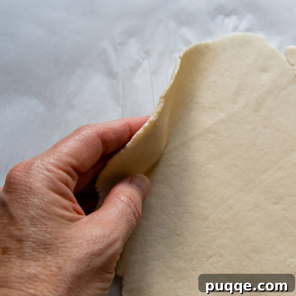 A hand demonstrating the perfect thinness of the rolled gluten-free dough.