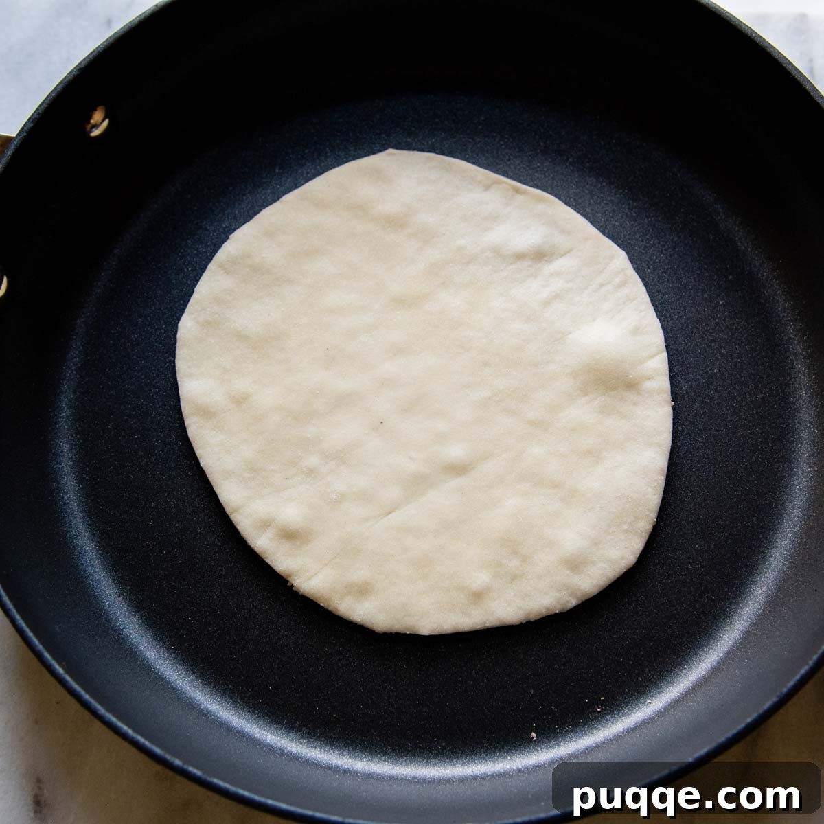 A gluten-free tortilla cooking in a hot skillet, just starting to show brown spots.