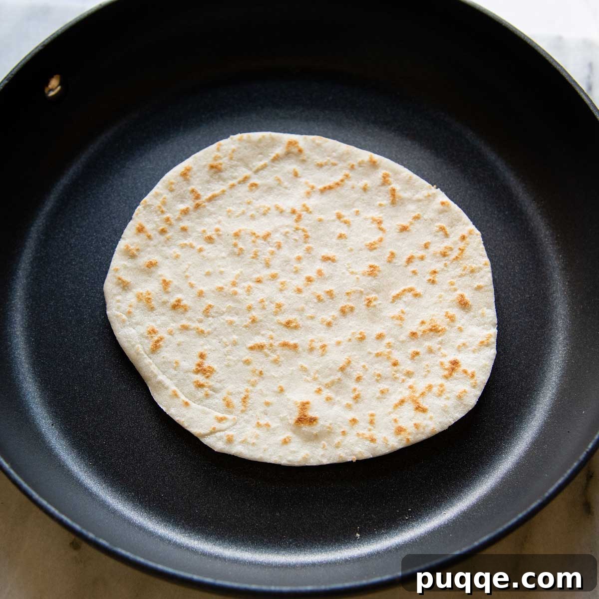 A gluten-free tortilla puffing up and cooking evenly in a nonstick skillet.