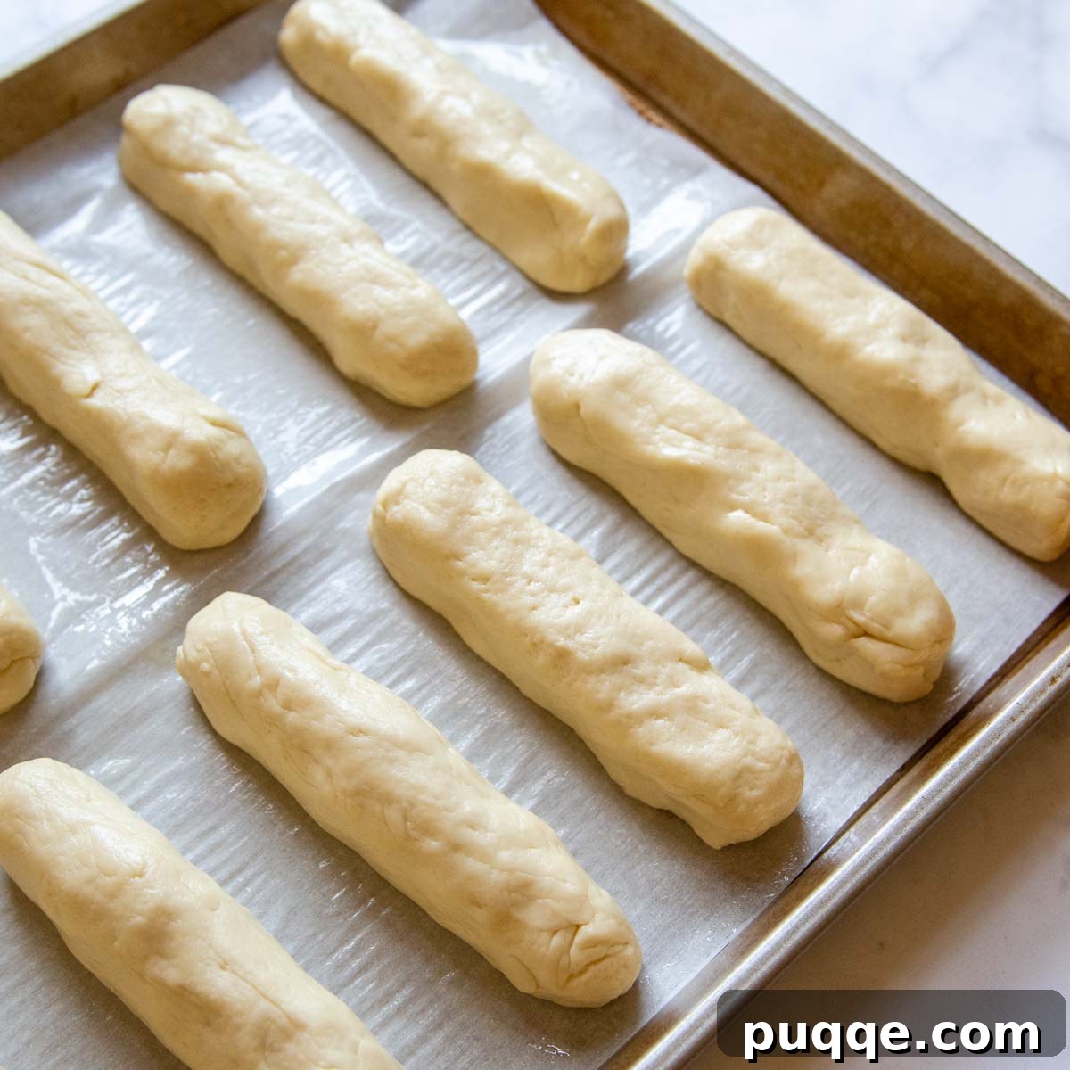 Gluten-free hot dog bun dough shaped into logs, neatly arranged in rows on a baking sheet, ready for the final rise.