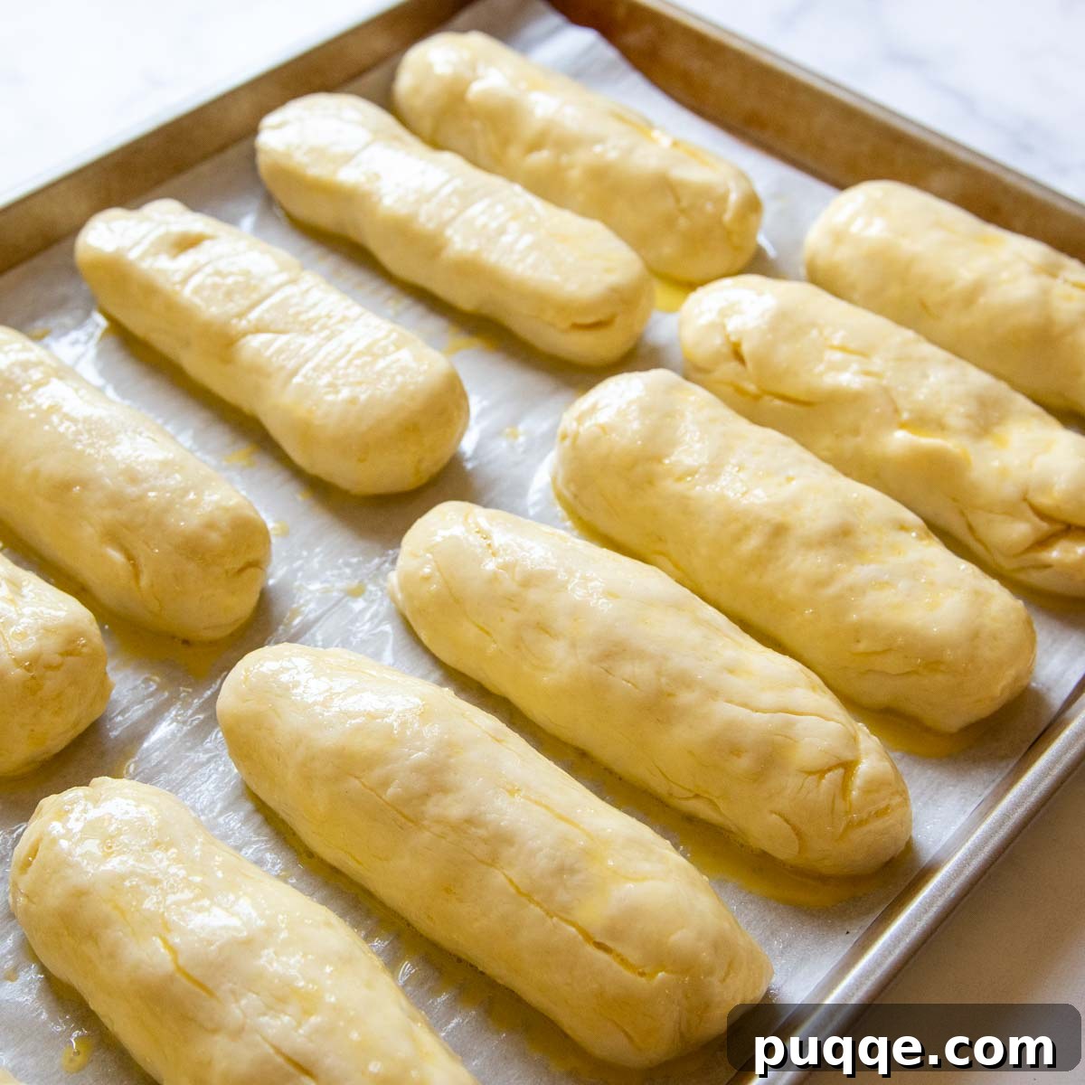 Golden-brown, perfectly risen gluten-free hot dog buns, glistening with an egg wash, cooling on a baking sheet.