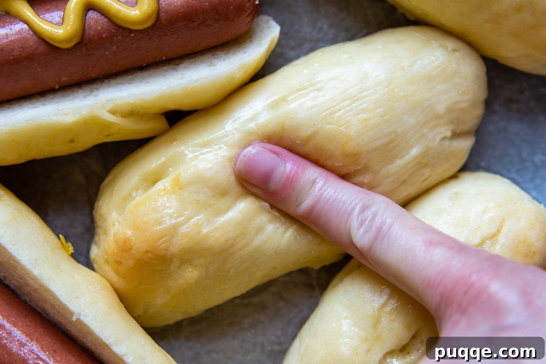 A gentle press on a freshly baked, soft gluten-free hot dog bun, showcasing its squishy and tender texture.
