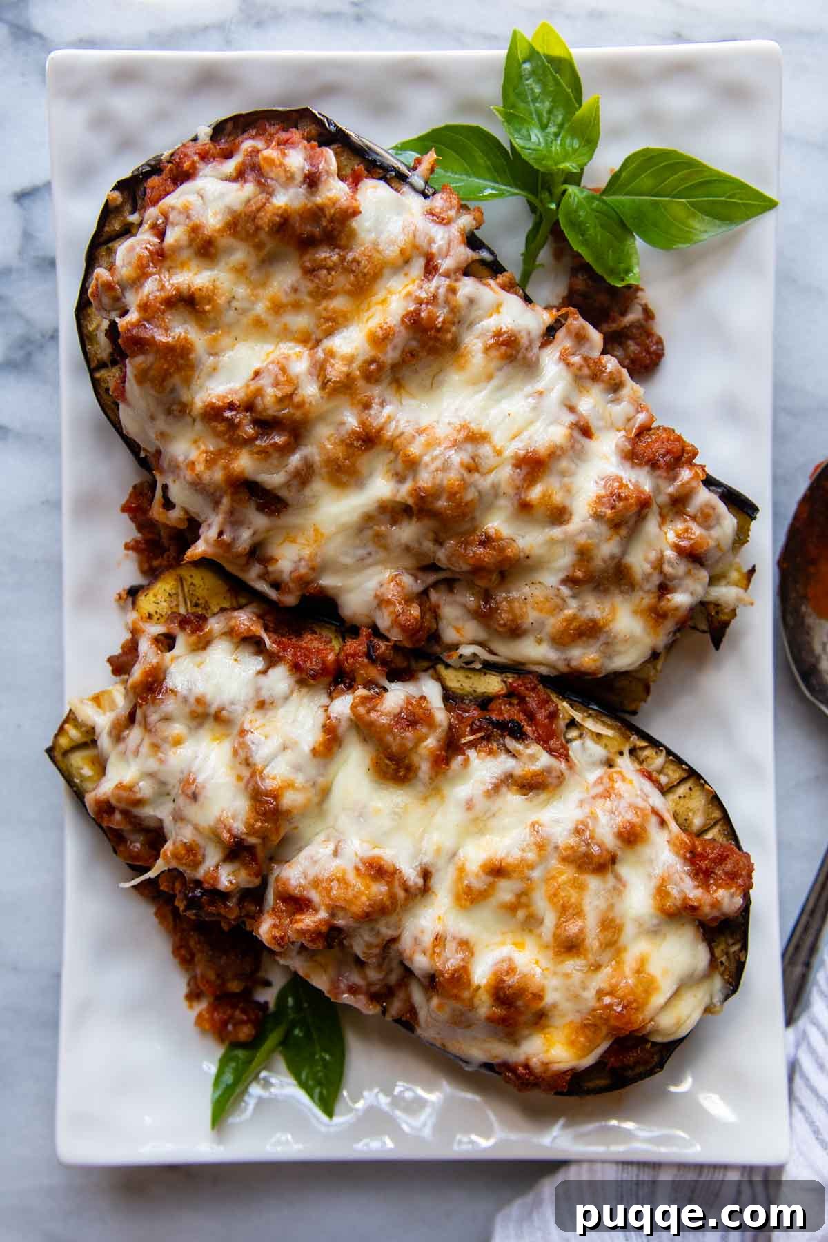 Hearty Gluten-Free Sausage-Filled Eggplant Boats 8 two eggplant boats on a white serving dish with a sprig of basil.