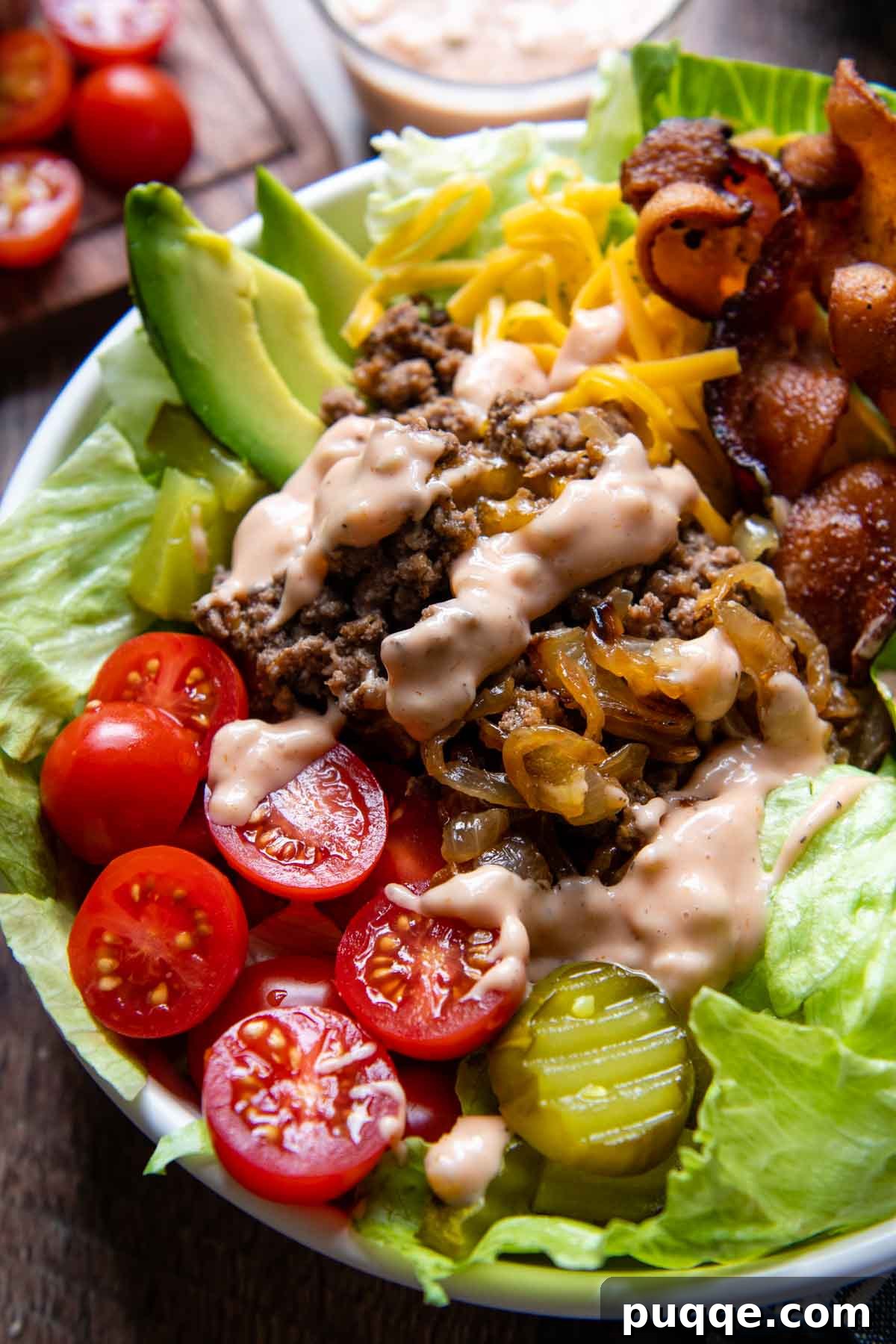 Gooey Cheeseburger Bowls with Crispy Bacon and Mystery Sauce 2 A vibrant burger bowl in a white serving bowl, richly drizzled with a creamy special sauce. It features seasoned ground beef, melted cheese, crisp lettuce, red onions, and other fresh toppings, offering a delightful bunless burger experience.