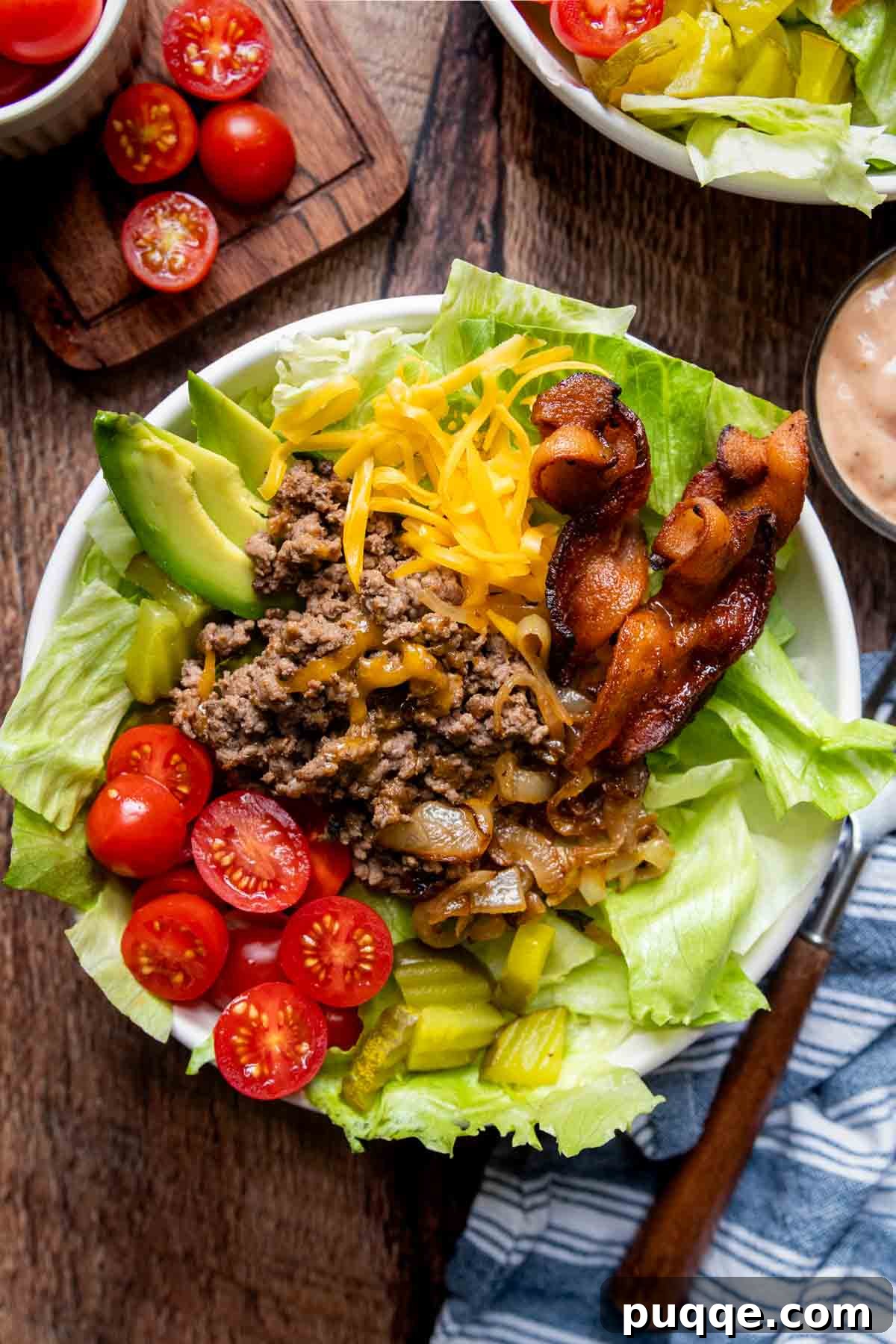 Gooey Cheeseburger Bowls with Crispy Bacon and Mystery Sauce 3 A generous white bowl brimming with fresh salad greens, topped with a flavorful ground beef and cheese mixture, and surrounded by a variety of classic burger fixings like tomatoes, pickles, and red onion, awaiting a delicious dressing.