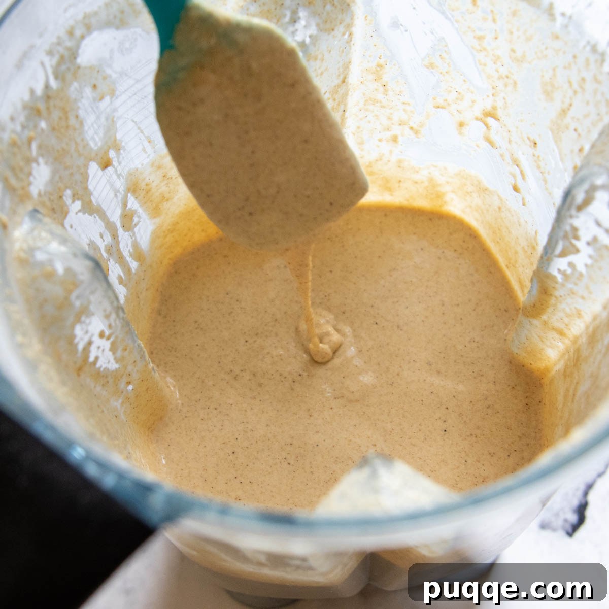 A spoon gently lifts a thick, well-rested oat flour pancake batter from a bowl, showcasing its improved texture.