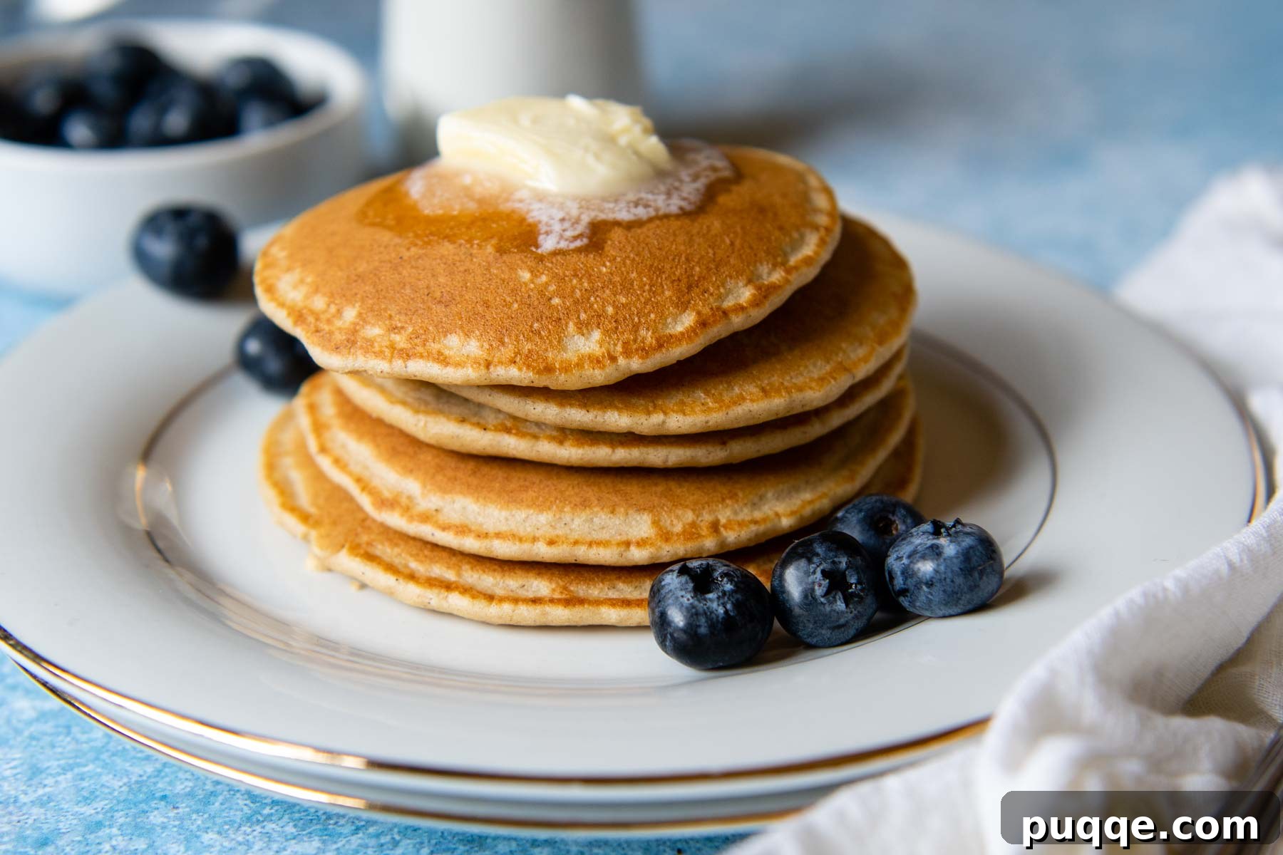 A stack of warm oat flour pancakes with a pat of butter melting invitingly on top, ready to be drizzled with syrup.