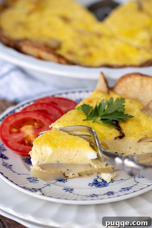Golden Potato Frittata 3 A fork cutting into a bite-sized piece of potato frittata, revealing the soft interior, with fresh sliced tomatoes resting beside it on a white plate.