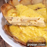 A spatula holding up a slice of potato frittata about to be taking out of a white pie dish.