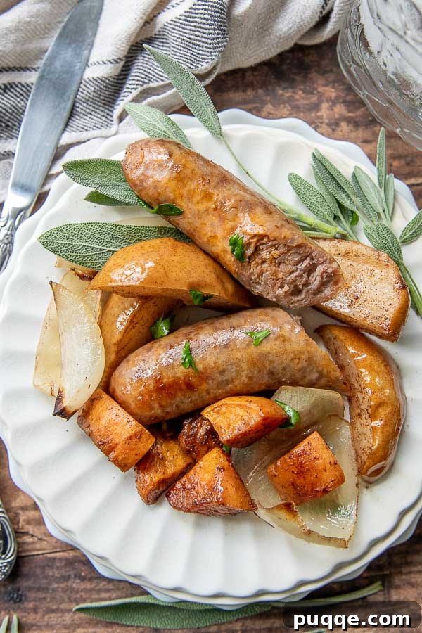 Sheet Pan Italian Sausage and Sweet Potato Bake 3 Baked Sausage dinner on a white plate with fresh sage laying next to it, showing a portion of sausage, sweet potatoes, and pears.