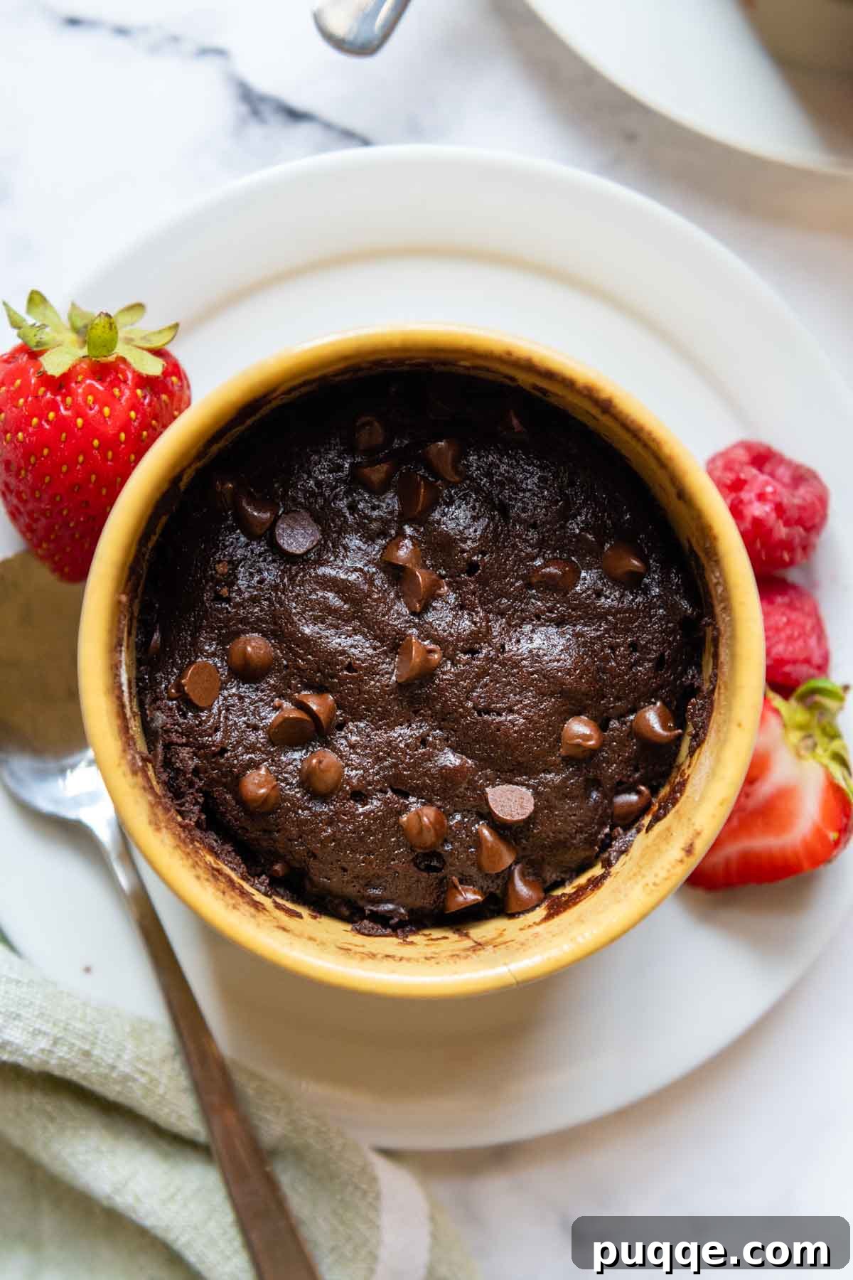 Effortless Gooey Fudgy Gluten-Free Mug Brownie 2 overhead shot of mug brownie in a yellow dish with berries next to it.
