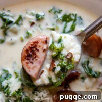 A spoon lifting out a bite of creamy kale and sausage soup.