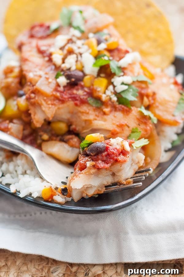 Quick Skillet Mexican Fish Dinner 7 A fork resting on a black plate with a bite of Mexican fish, rice, and fresh cilantro, showcasing the vibrant flavors.