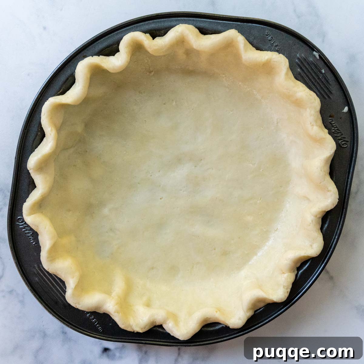 An unbaked pie crust, perfectly crimped and ready for the freezer, sitting in a metal pie pan.