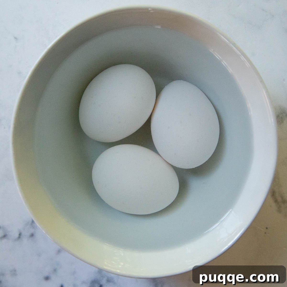 Three whole eggs soaking in a bowl of warm water to reach room temperature quickly.
