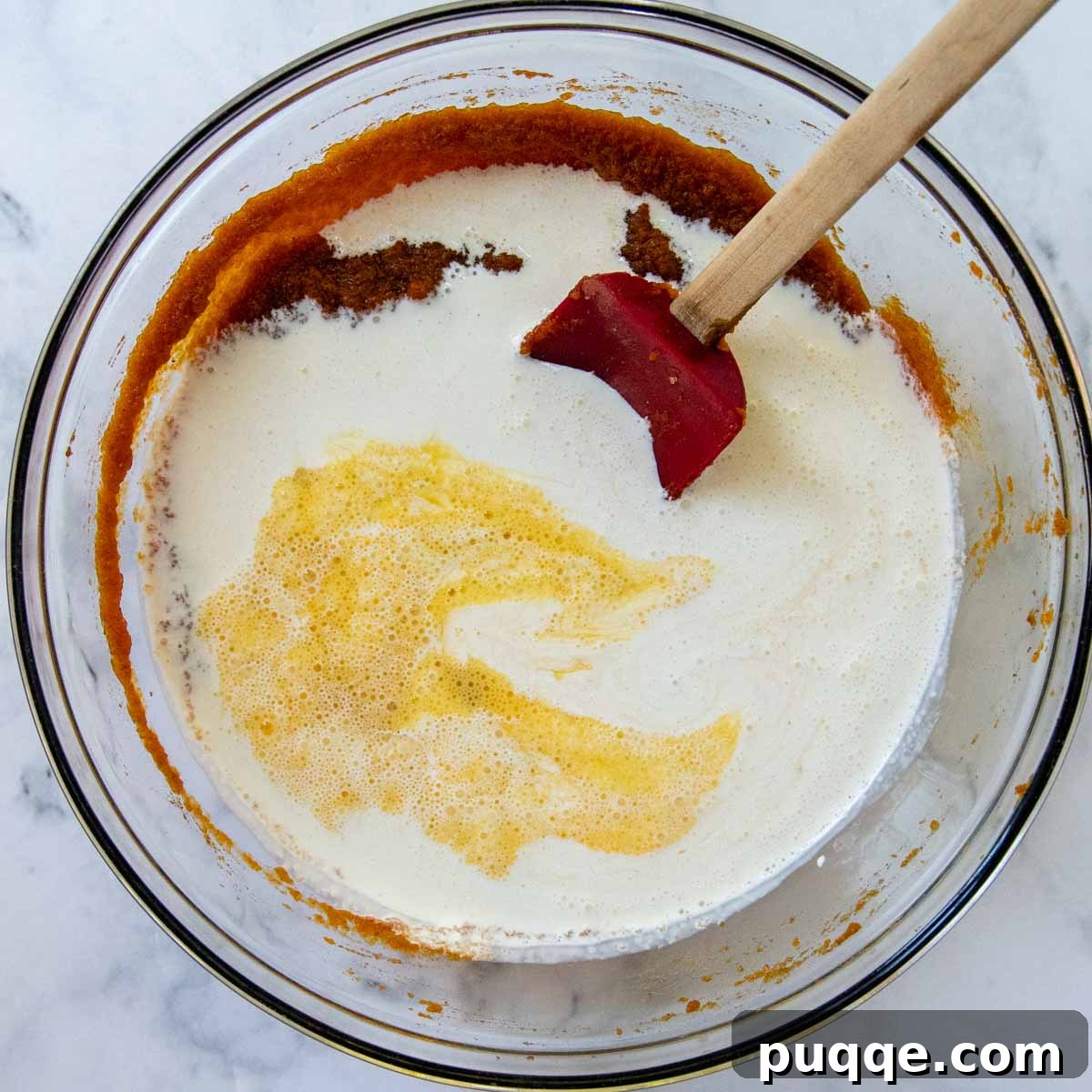 Heavy cream and lightly beaten eggs being gently stirred into the pumpkin, brown sugar, and spice mixture in a large bowl.