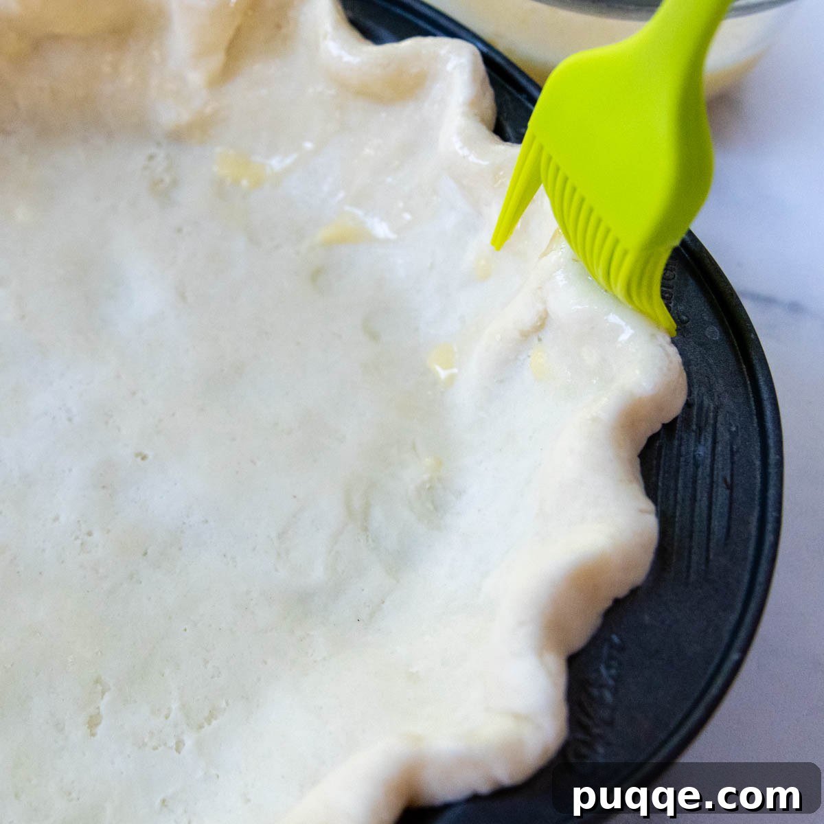 A pie crust being brushed with an egg wash mixture to create a shiny, golden finish.