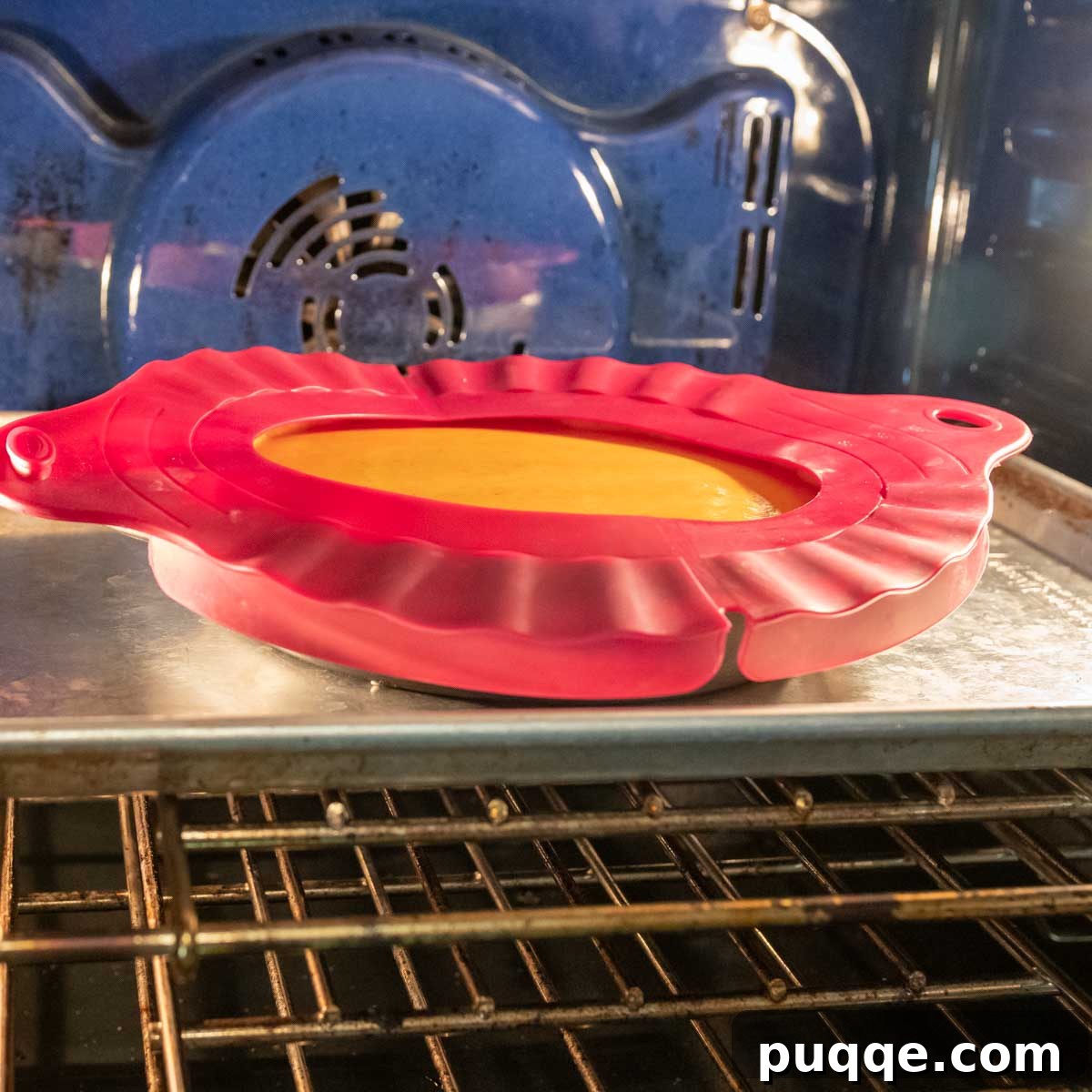 A pumpkin pie in the oven with a pie shield protecting the crust edges from over-browning.