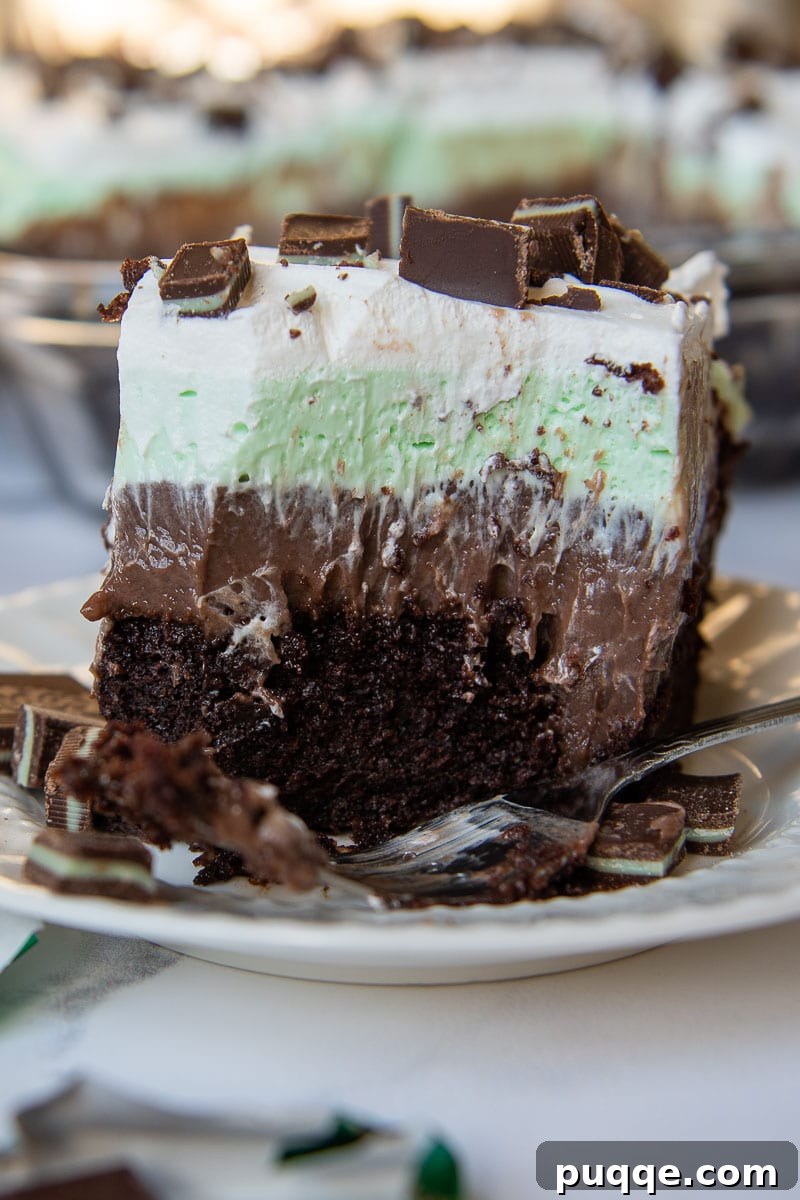 A large bite taken out of a slice of Andes Mint Chocolate Pudding Poke Cake, with a fork resting on the plate, highlighting the moist cake, creamy pudding, and mint topping.