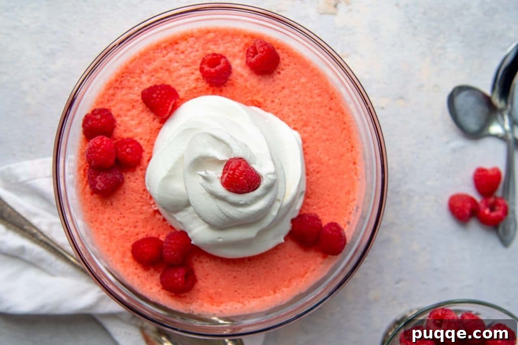 An overhead shot of a creamy pink Jello salad in a glass bowl, surrounded by fresh raspberries.