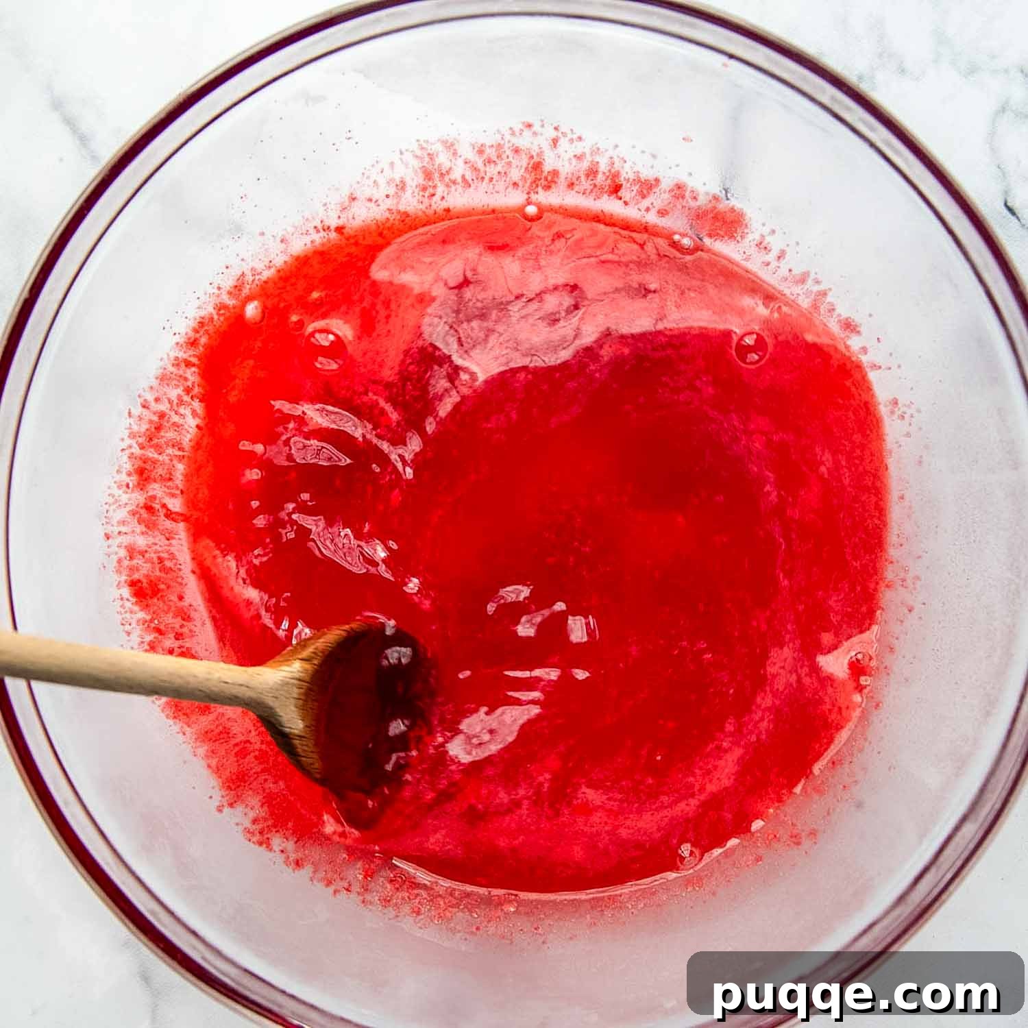 Raspberry Jello dissolved in boiling water, steaming slightly in a mixing bowl.