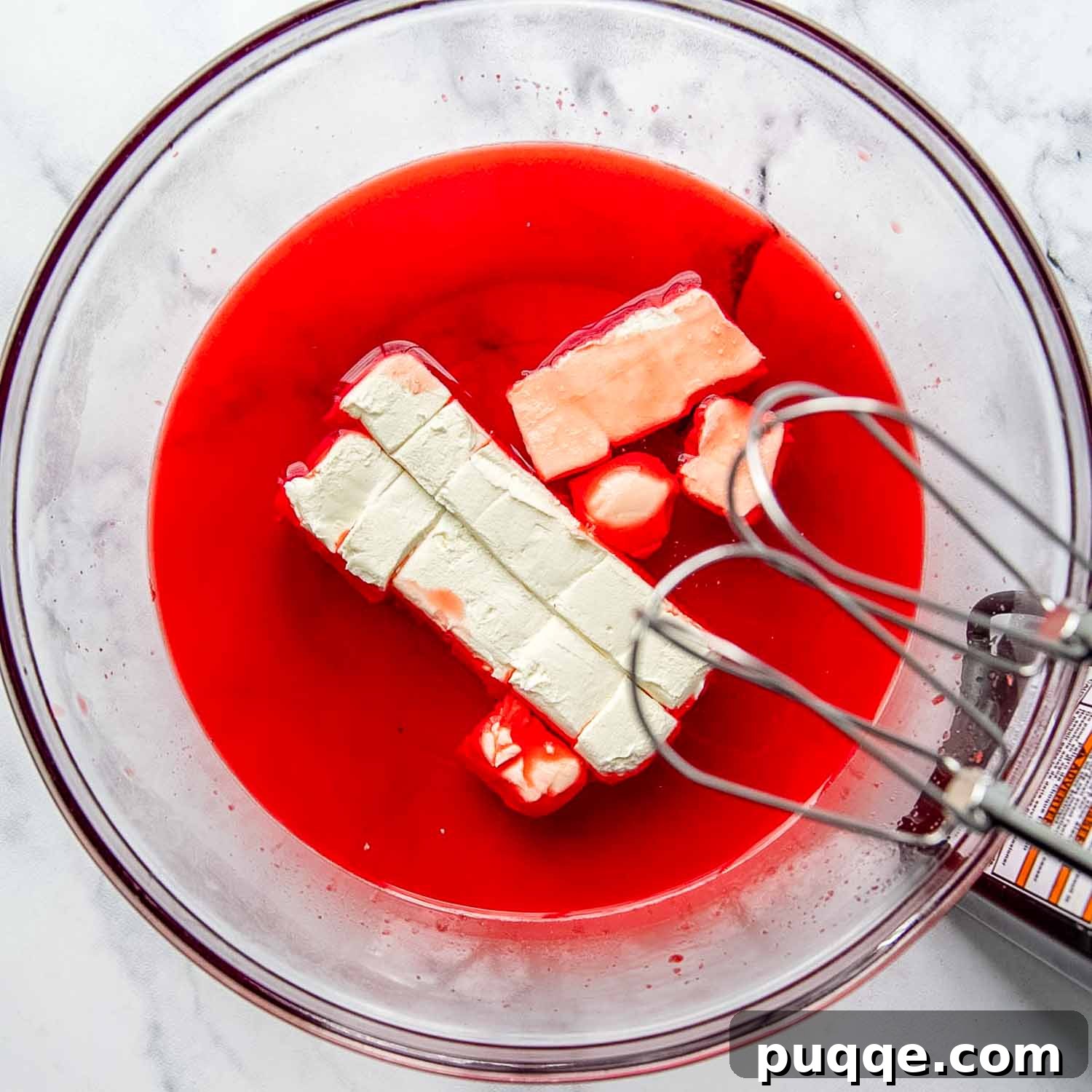 Softened cream cheese being blended into dissolved Jello with a hand mixer in a large bowl.