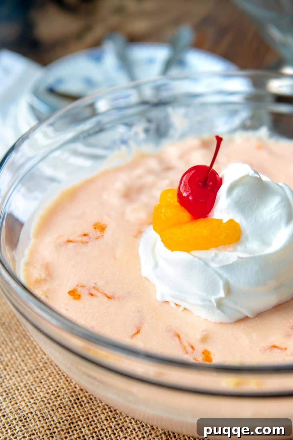 An orange Jello salad with cream cheese in a glass bowl, garnished with bright red cherries on top.