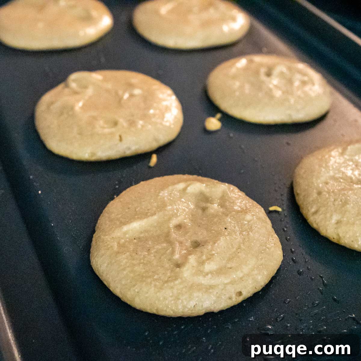 Pumpkin pancake batter cooking on a hot griddle, showing the beginnings of bubbles forming.