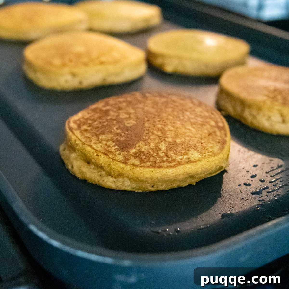 Golden-brown pumpkin oatmeal pancakes cooking on a griddle, indicating they are nearly ready to serve.