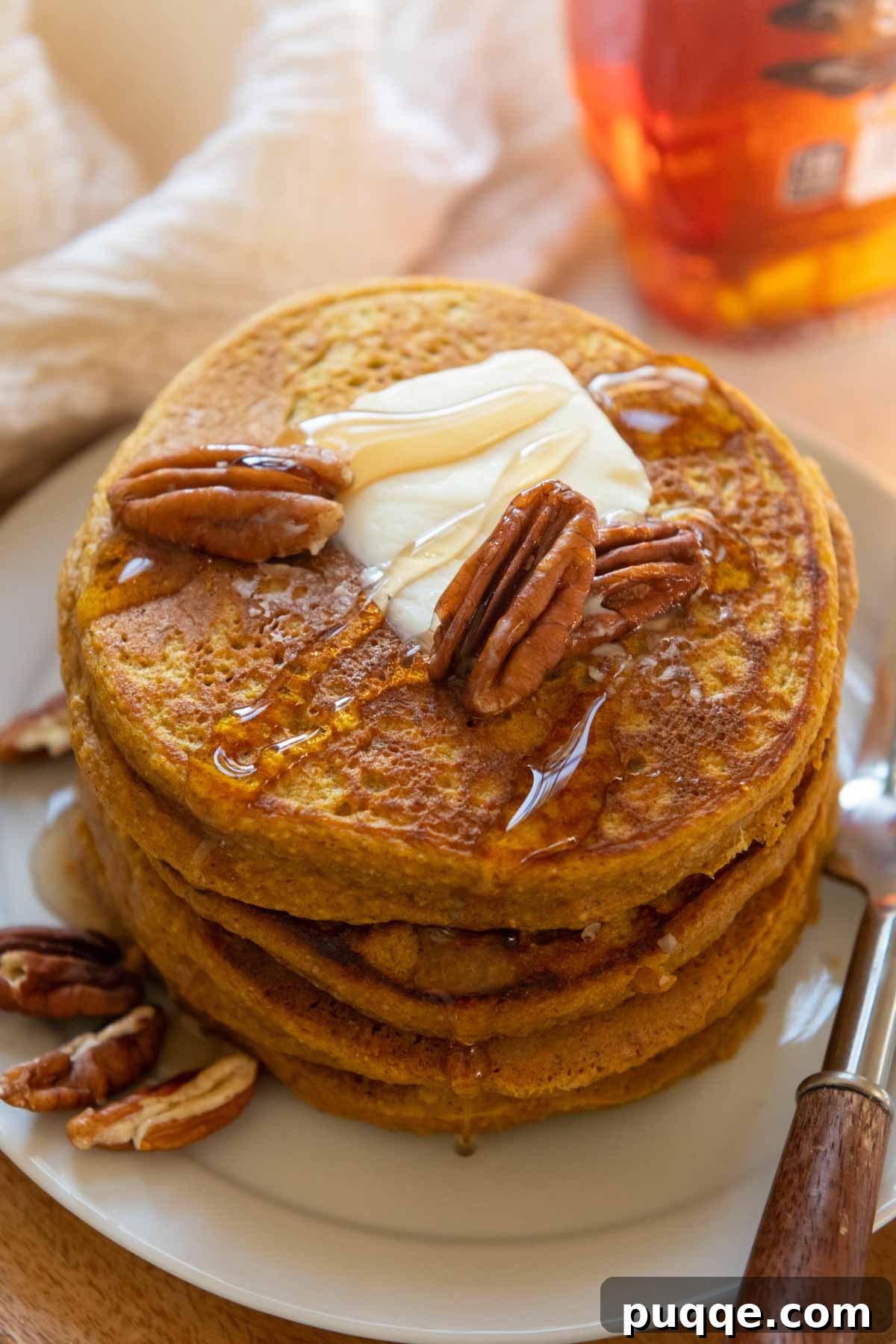 A beautifully stacked plate of fluffy pumpkin oatmeal pancakes, generously drizzled with maple syrup, ready to be enjoyed.