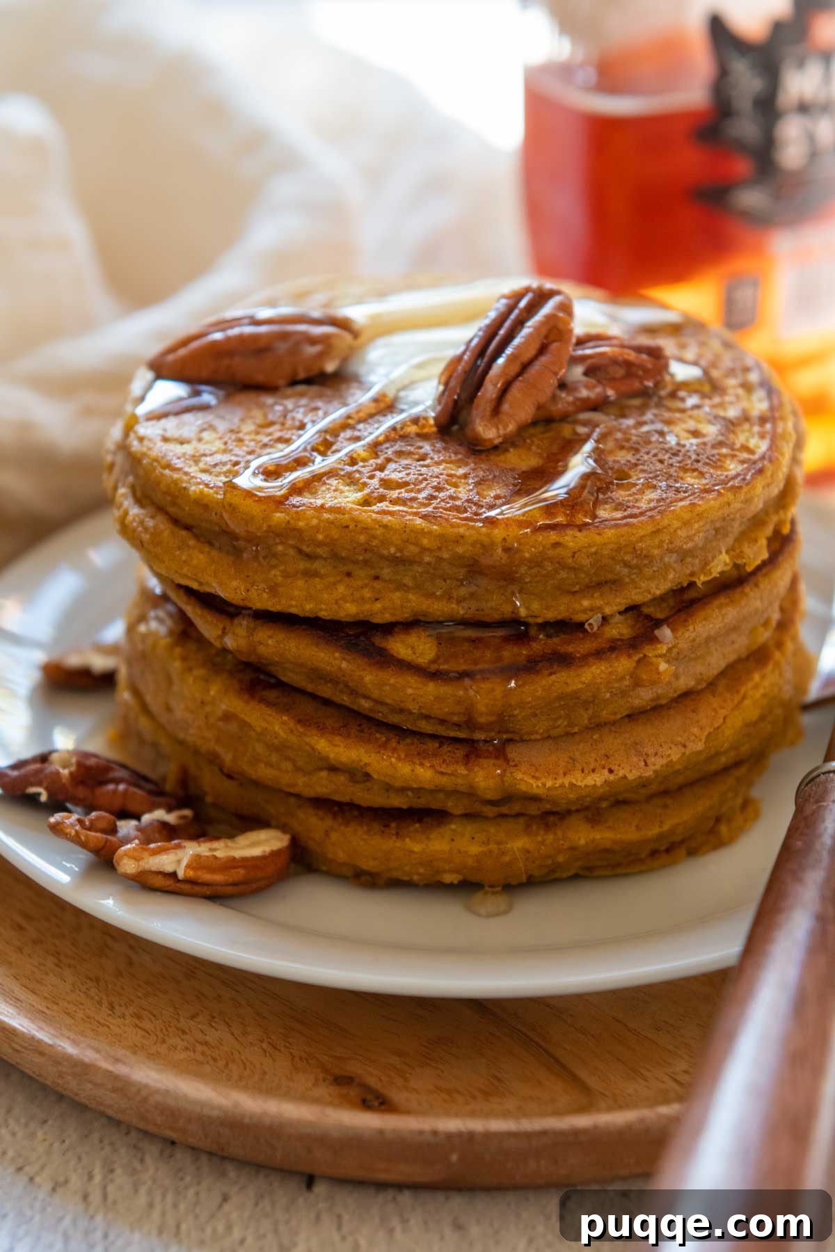 A close-up of a stacked plate of pumpkin oatmeal pancakes, adorned with pecans and a dollop of butter, showcasing their rustic appeal.