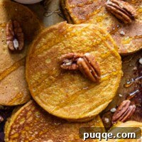 Overhead shot of pancakes laying on a pan with syrup and nuts.