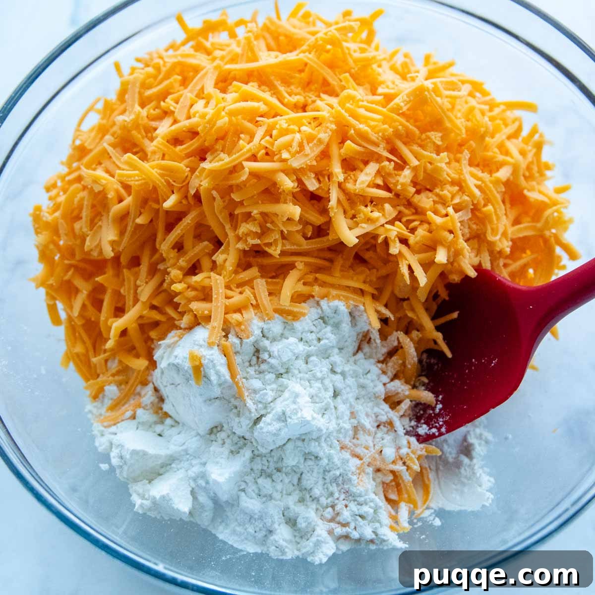 A glass bowl containing gluten-free flour mixed with shredded cheddar cheese, ready for the next ingredients.