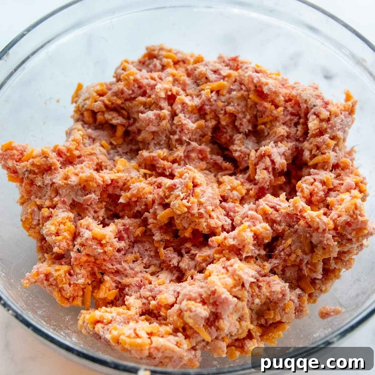 A glass bowl filled with the fully combined ground sausage mixture, including flour, cheese, and milk, ready for shaping.