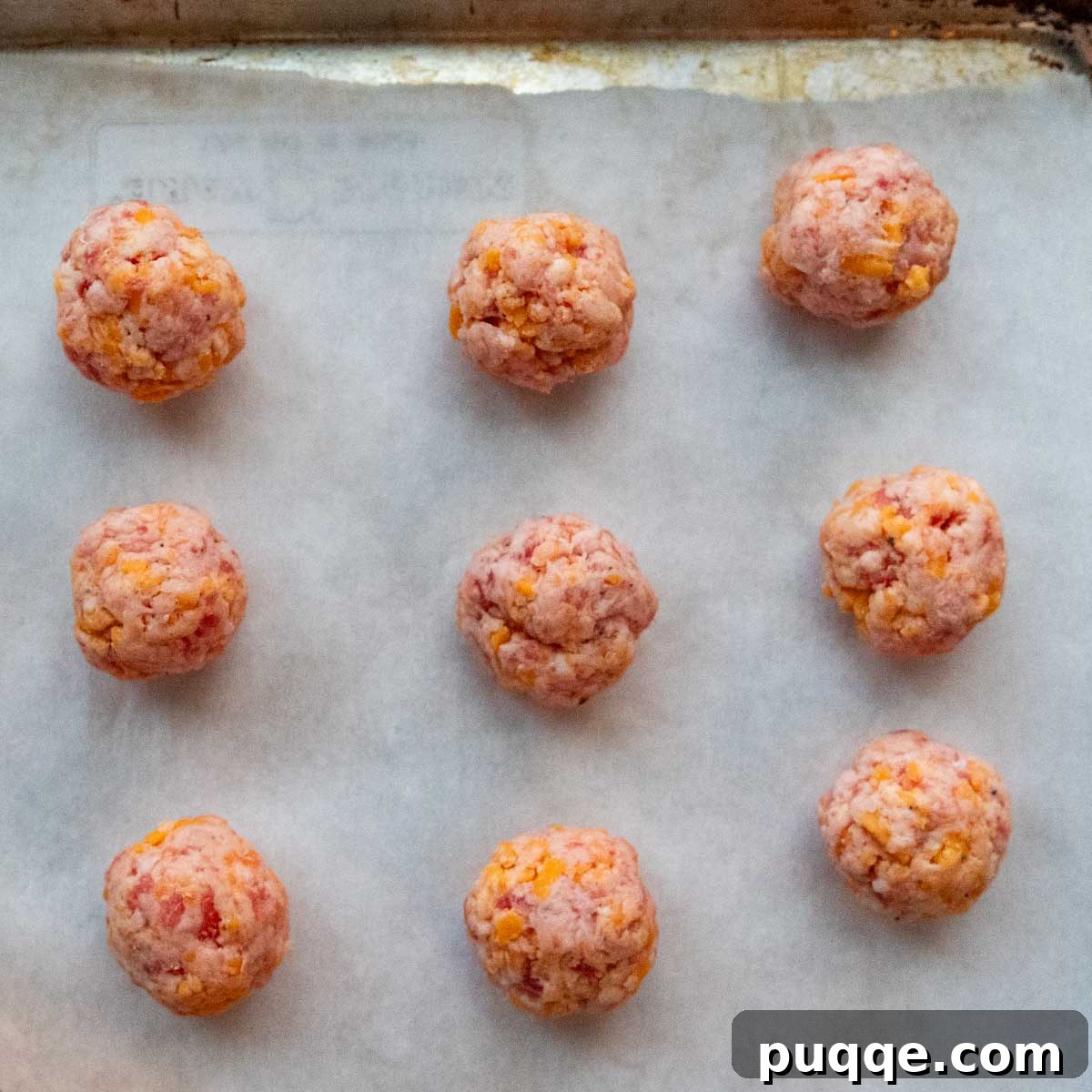 Raw gluten-free sausage balls, perfectly shaped and arranged on a parchment-lined baking sheet, ready for baking or freezing.