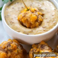 A gluten-free sausage ball being dipped into a small bowl of spicy sweet hot honey mustard sauce.
