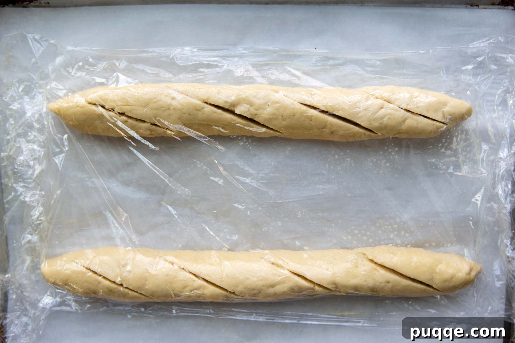 Two shaped gluten-free baguettes with diagonal slashes, ready for the rising process.
