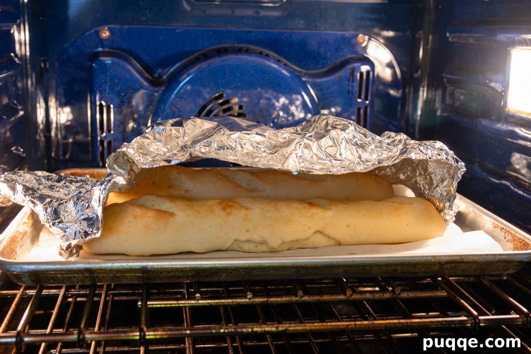 Gluten-free French bread baking in the oven, with foil loosely tented over to prevent over-browning.