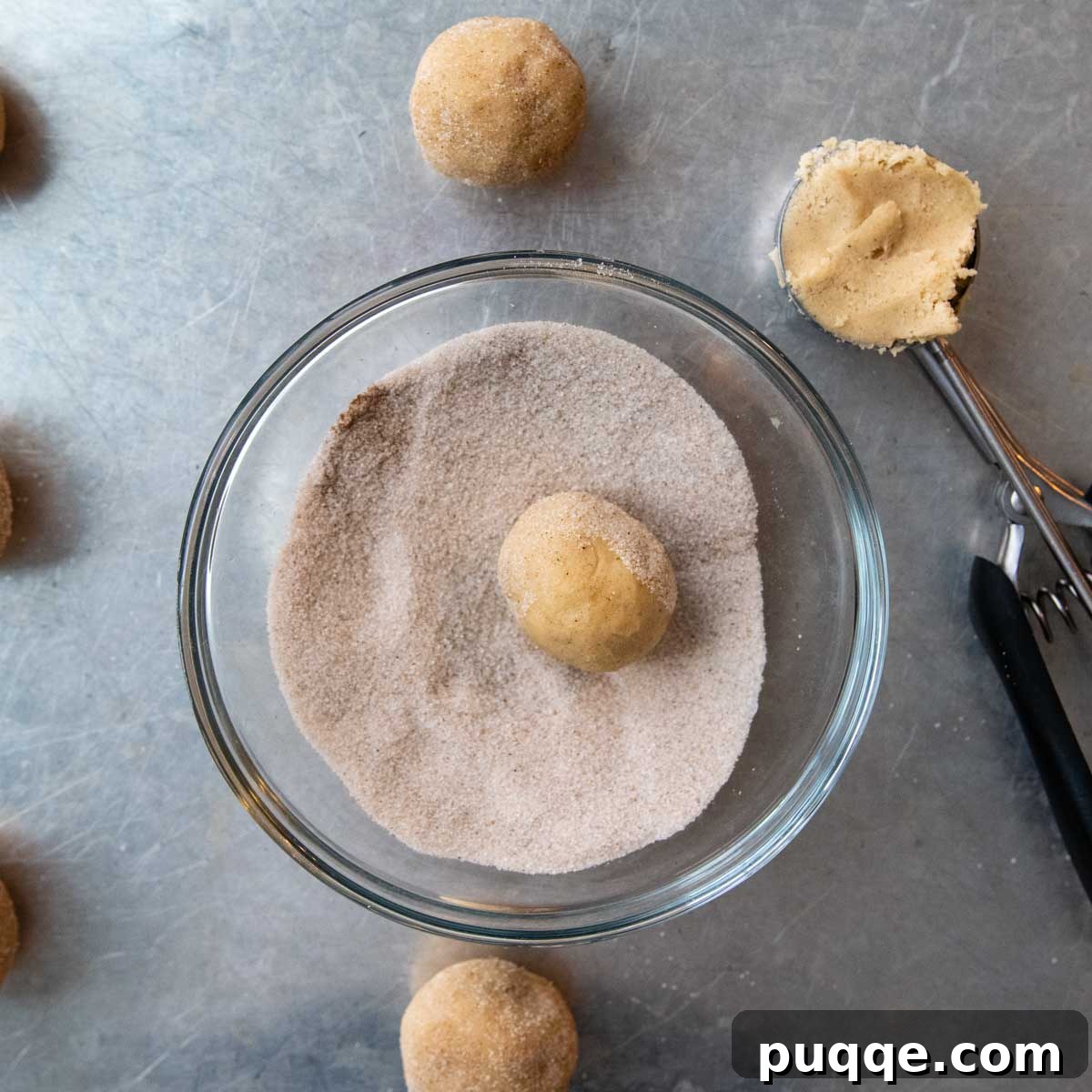 Gluten-free snickerdoodle cookie dough balls, generously coated in cinnamon sugar, ready for baking.