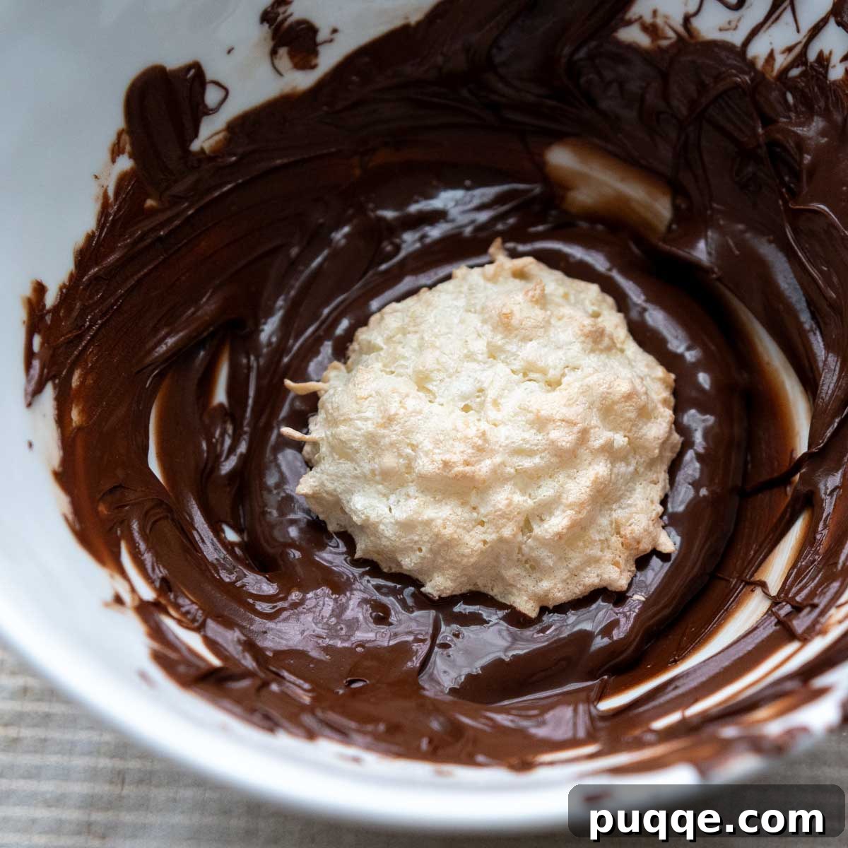 Featherlight Gluten-Free Coconut Delights 9 a single coconut macaroon being placed into a bowl of melted chocolate.