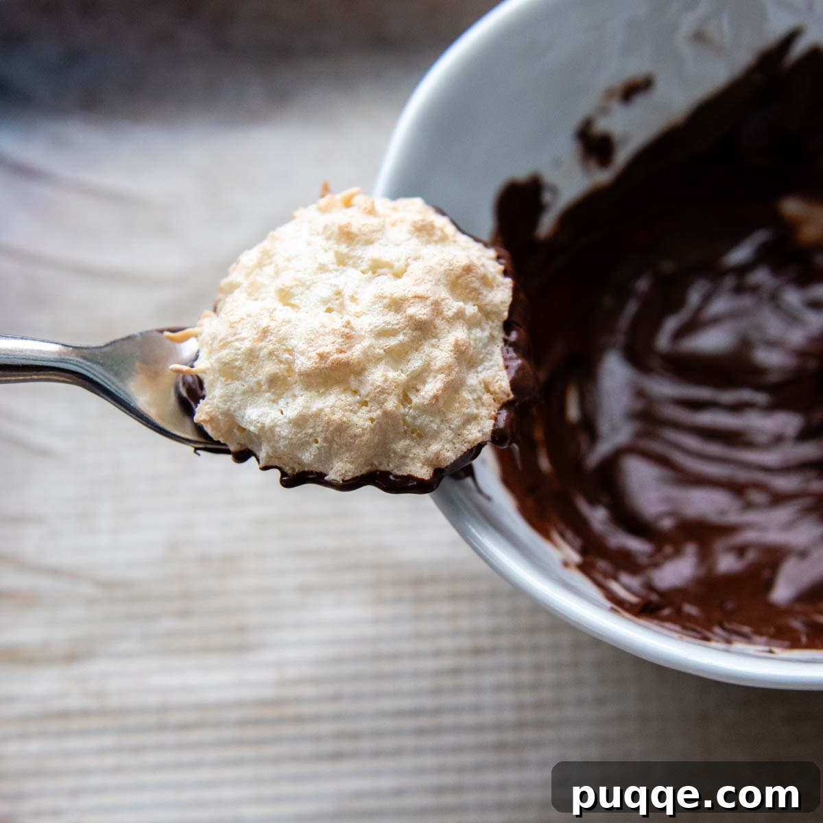 Featherlight Gluten-Free Coconut Delights 10 a chocolate-dipped macaroon being lifted out of a bowl with a fork.