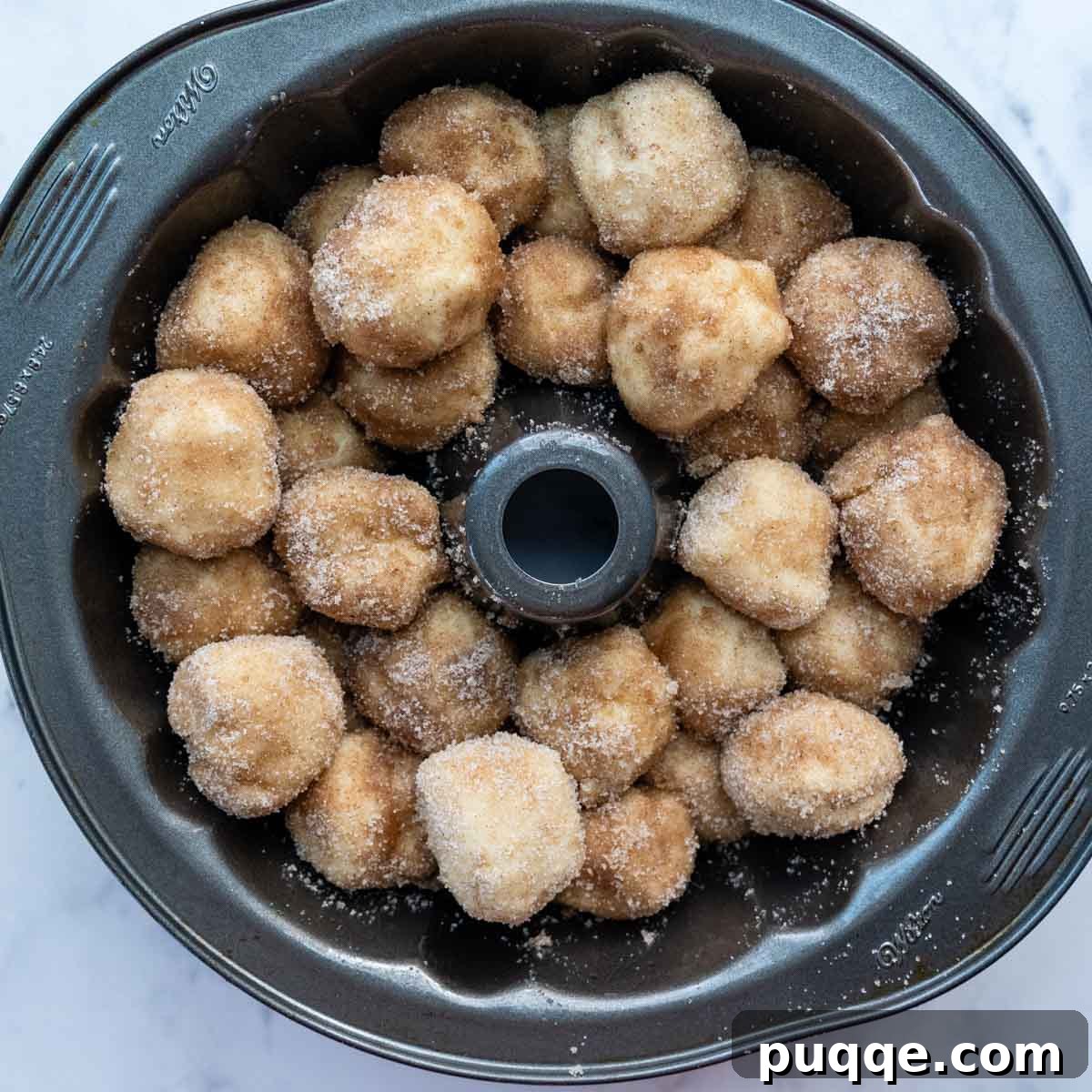 Melt-in-Your-Mouth Gluten Free Sticky Pull Apart Bread 8 Unbaked cinnamon-coated dough balls neatly arranged in layers within a bundt cake pan, ready for rising.