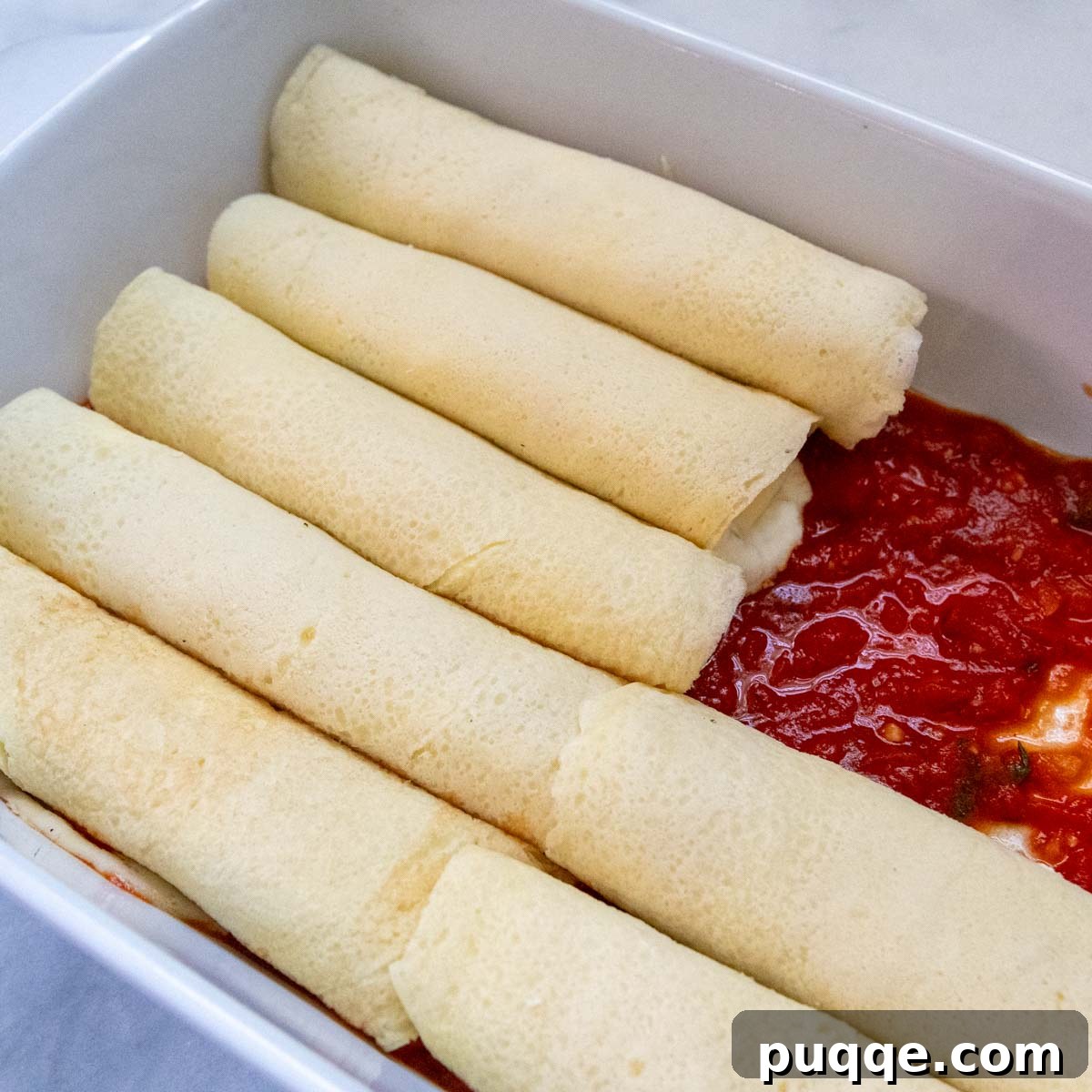 Effortless Homemade Gluten-Free Manicotti with Tender Crepe Shells 10 unbaked manicotti shells neatly lined up in a casserole dish, topped with sauce.
